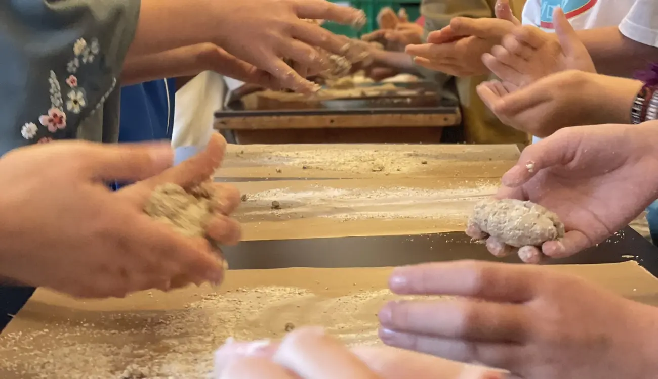 Schülerinnen und Schüler formen am Tisch kleine Brote aus Teig