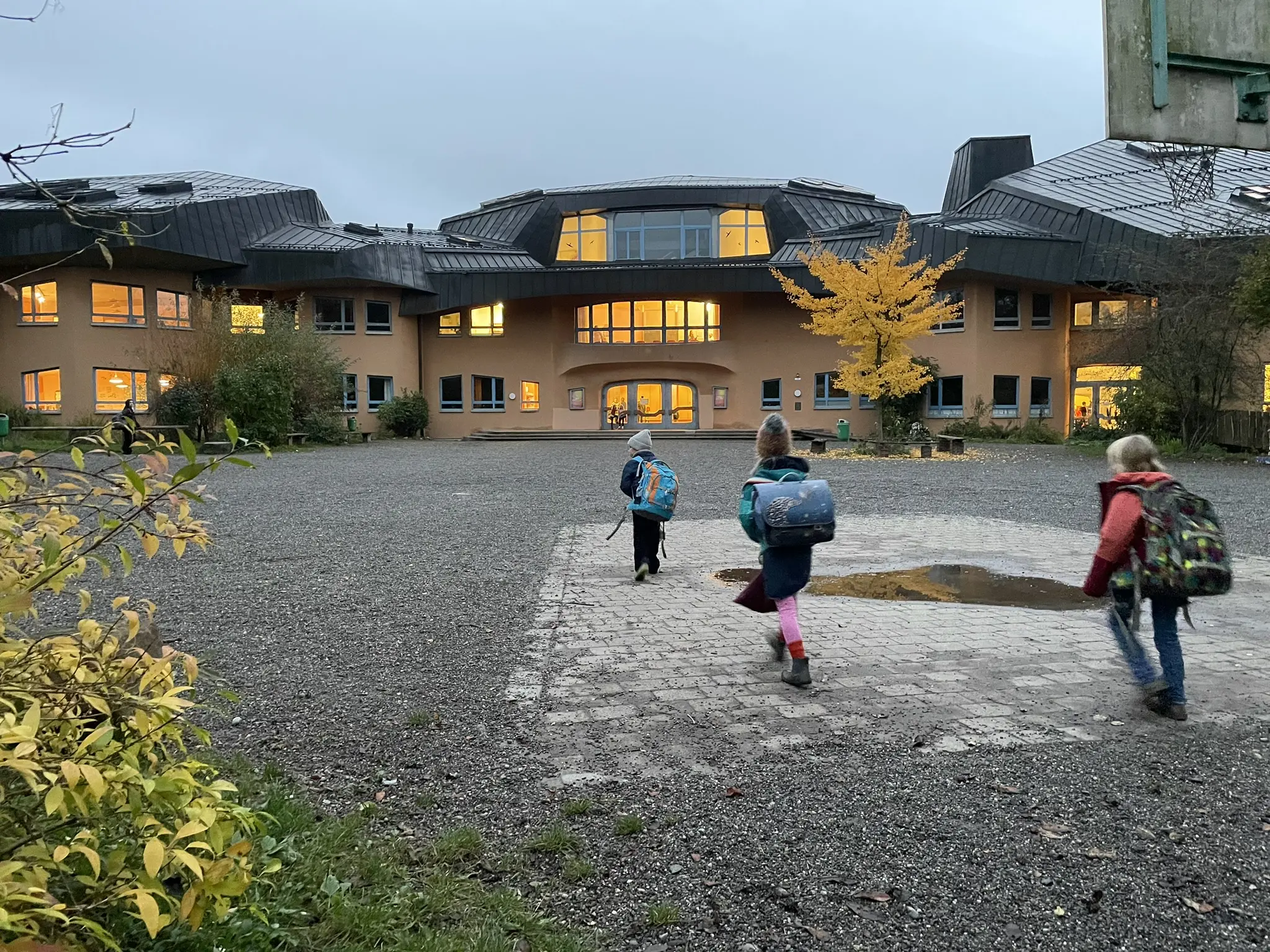 Kinder mit Schulranzen laufen über den Schulhof zum Schulgebäude
