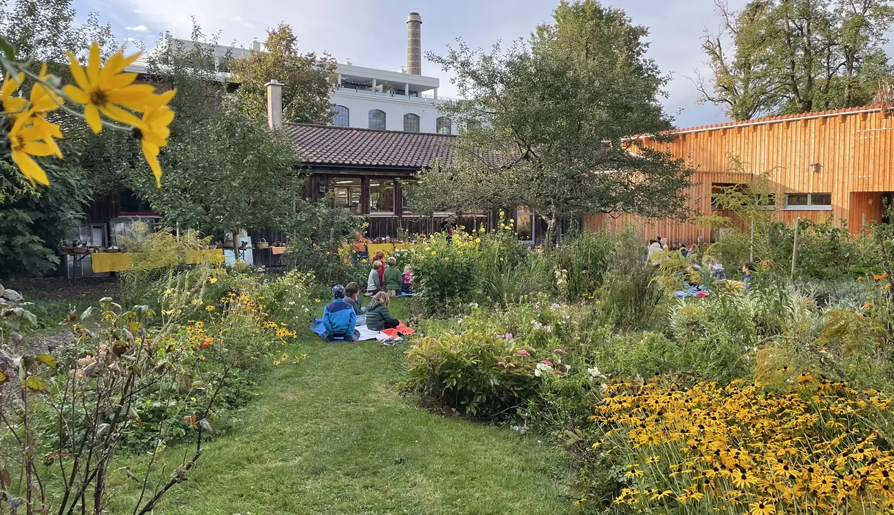 Kinder sitzen zwischen blühenden Beeten im Schulgarten im Gras