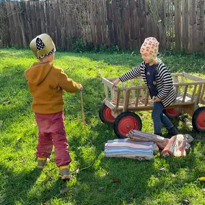 Zwei Kinder spielen auf der Wiese mit einem hölzernen Leiterwagen
