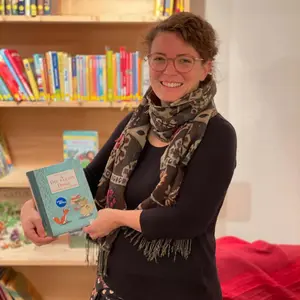 Eine Lehrerin hält lächelnd ein Buch vor einem Bücherregal