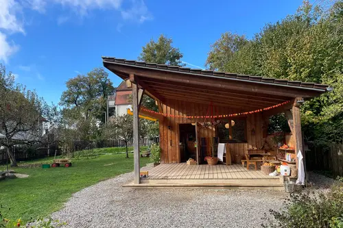 Überdachter Holzunterstand der Naturgruppe mit Herbstschmuck, davor Kiesplatz und Wiese