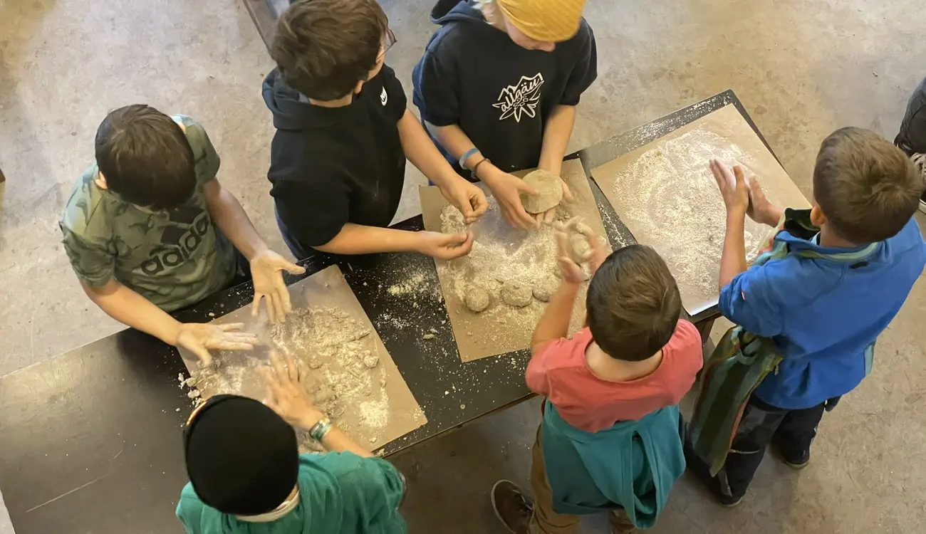 Kinder kneten an einem Tisch Teig auf bemehltem Backpapier