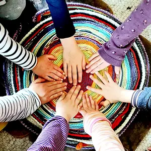 Viele Kinderhände liegen gemeinsam auf einem bunten geflochtenen Teppich