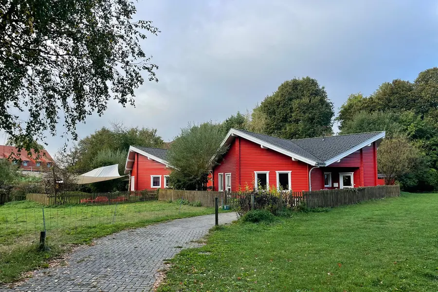 Rotes Holzhaus des Kindergartens mit Wiese und gepflastertem Weg