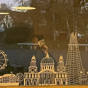 Fenster im Klassenzimmer mit einer aufgemalten Stadtsilhouette mit Riesenrad, davor ein Buch und eine Pflanze