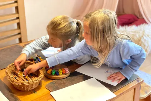 Zwei Mädchen malen am Tisch mit Wachsmalblöckchen und Wachsmalstiften