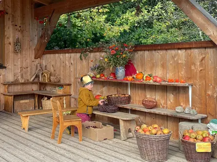 Ein Kind sortiert Äpfel unter dem herbstlich geschmückten Holzdach im Kindergartengarten