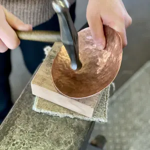 Eine Kupferschale wird mit dem Hammer auf einem Amboss getrieben