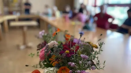 Ein Wiesenblumenstrauß im Glas auf einem langen Tisch