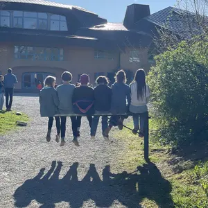 Schülerinnen und Schüler sitzen auf einem Geländer vor dem Schulgebäude in der Sonne