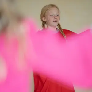 Ein Mädchen in Rot bei der Eurythmie, im Vordergrund ein bewegtes rosa Tuch