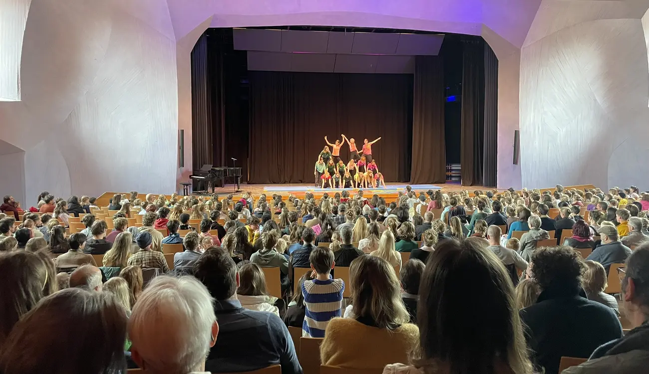 Schülerinnen und Schüler zeigen eine Menschenpyramide auf der Bühne vor vollem Saal