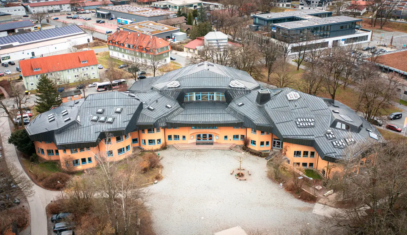 Luftaufnahme des Schulgebäudes mit seinen grauen, vieleckigen Dächern und dem Schulhof