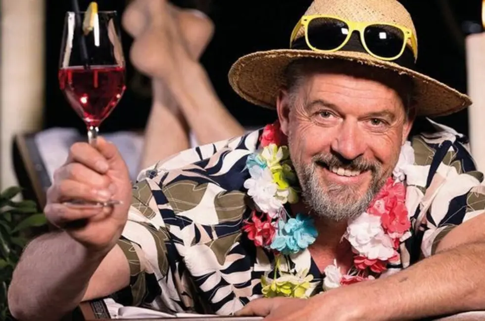 Ein Mann mit Strohhut, Hawaiihemd und Blumenkette prostet mit einem Glas zu
